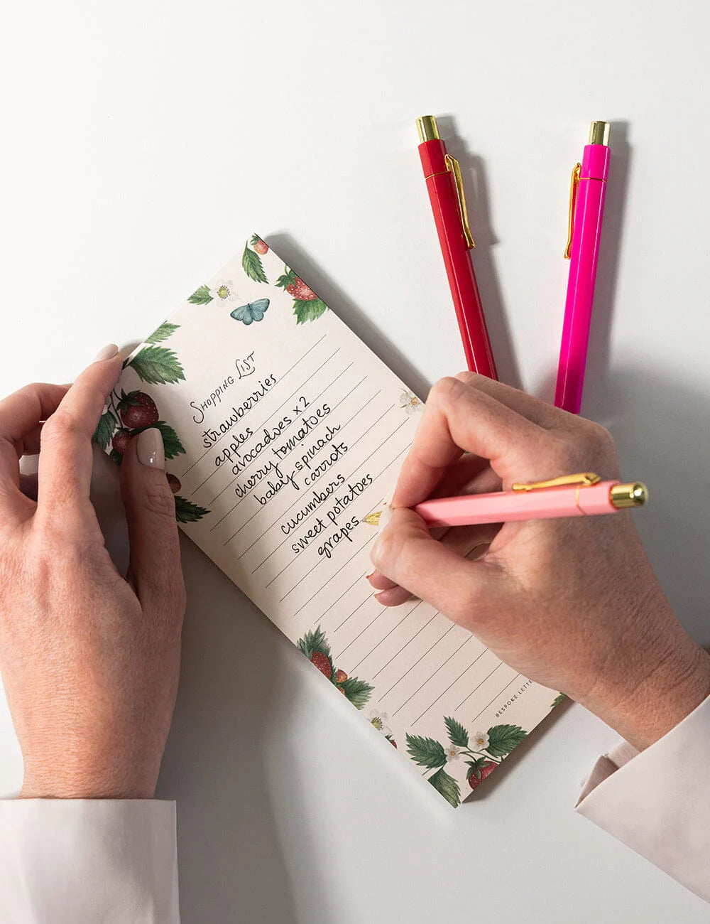 Person writing in a floral notebook with two pens on a white background