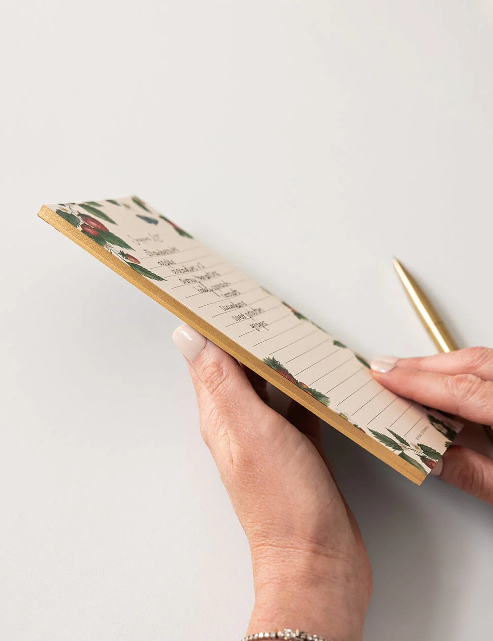 Hand holding a floral notebook with a pen on a light background