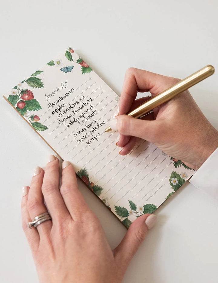 Person writing in a floral notebook with a gold pen on a white surface