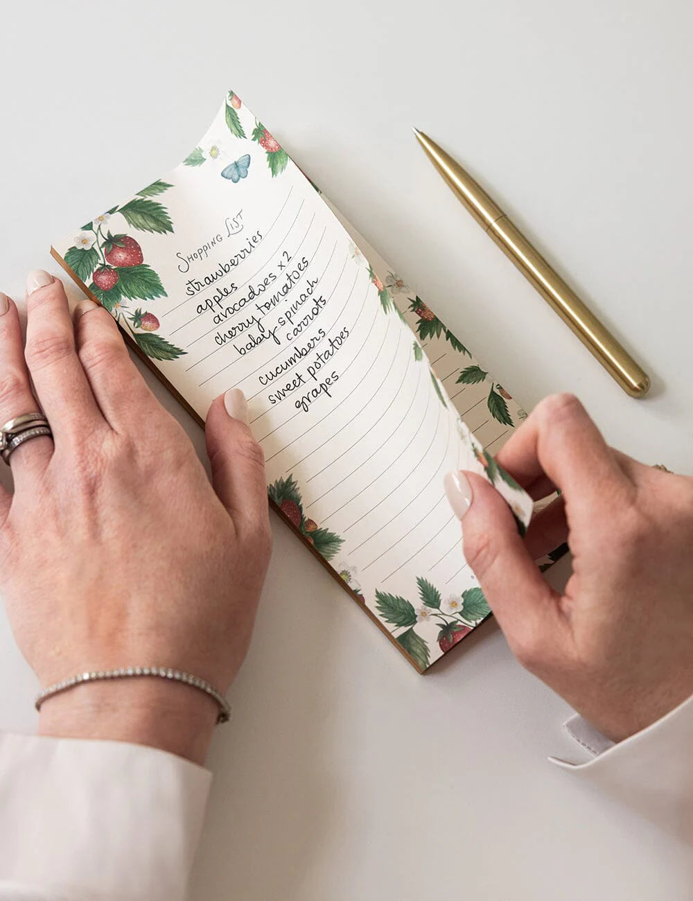 Person holding a notebook with floral design and a pen on a light surface