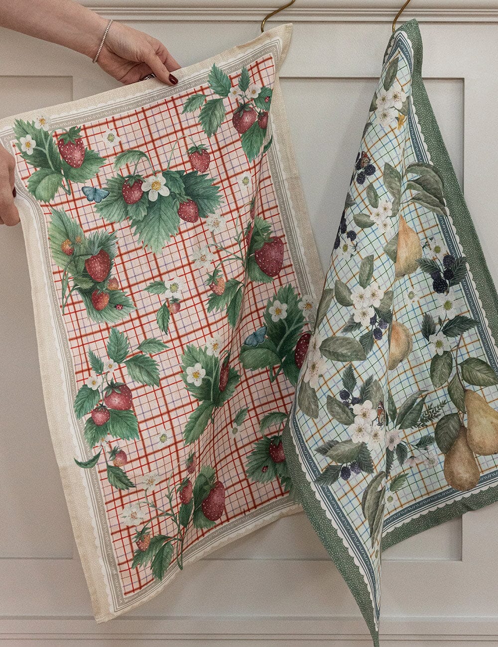 Two patterned towels with fruit designs hanging against a neutral background