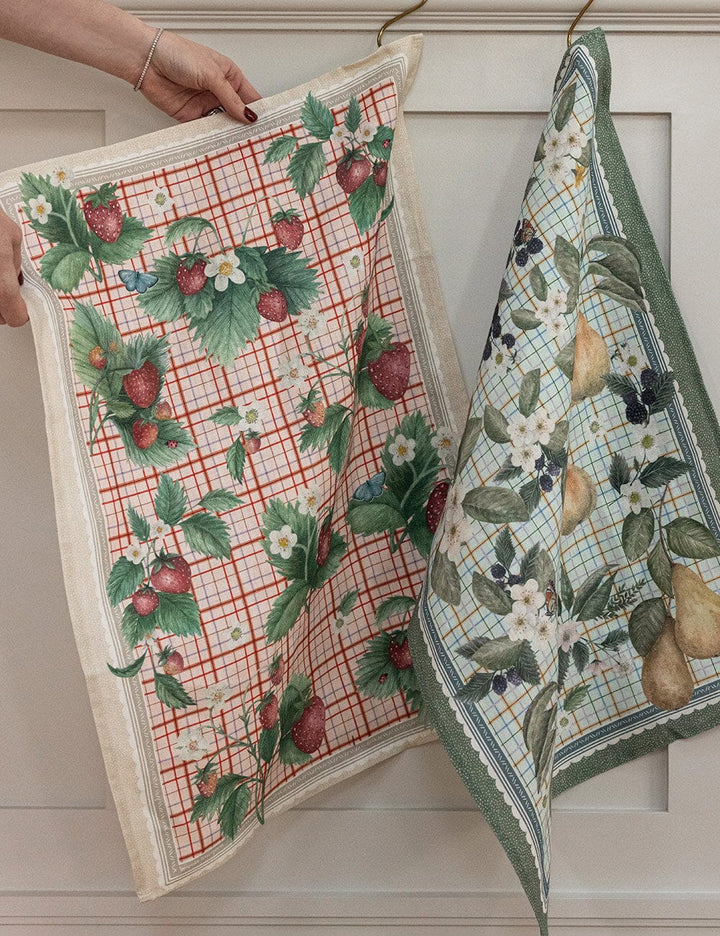 Two patterned towels with fruit designs hanging against a neutral background