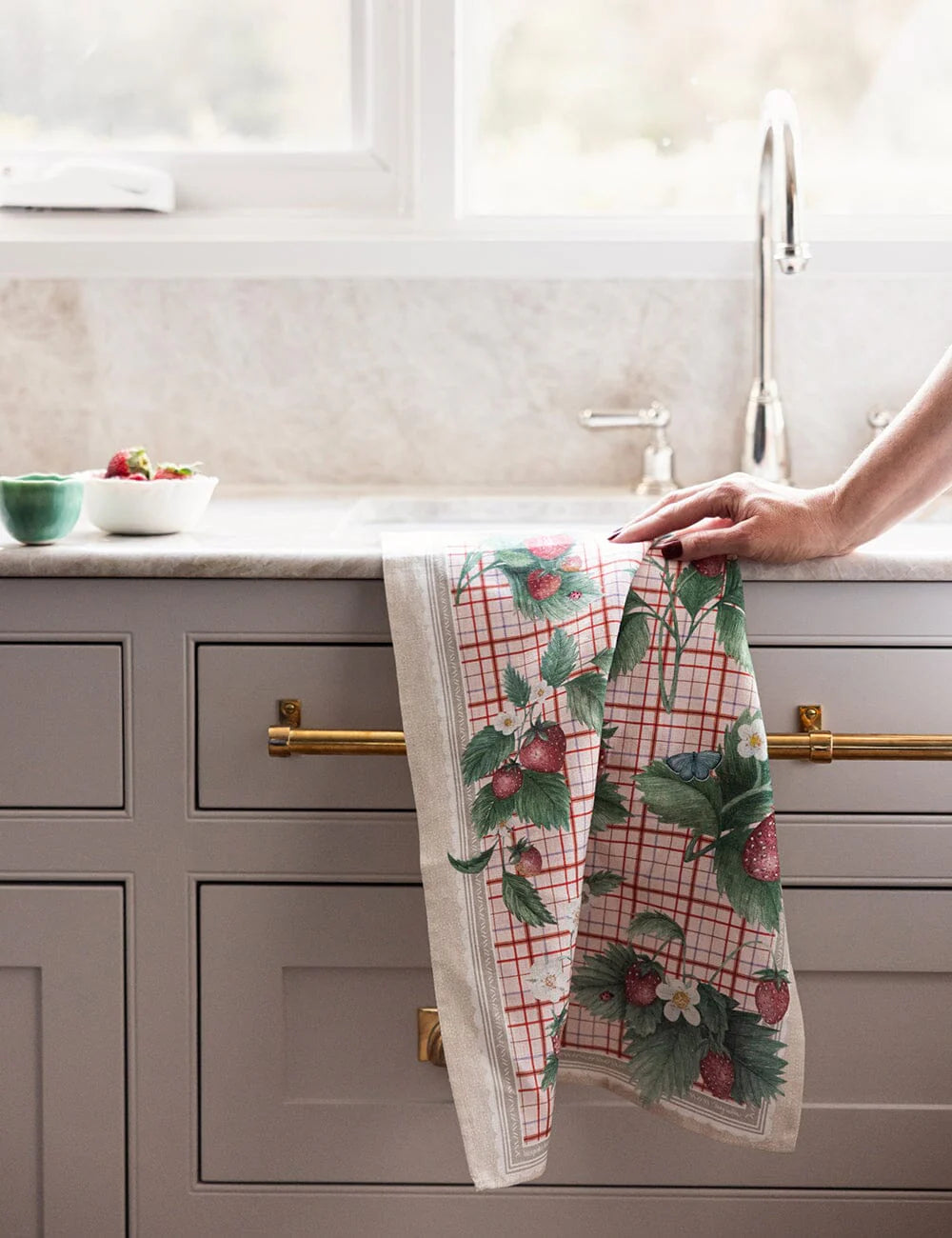 Person hanging a decorative kitchen towel with strawberry pattern on a kitchen counter.