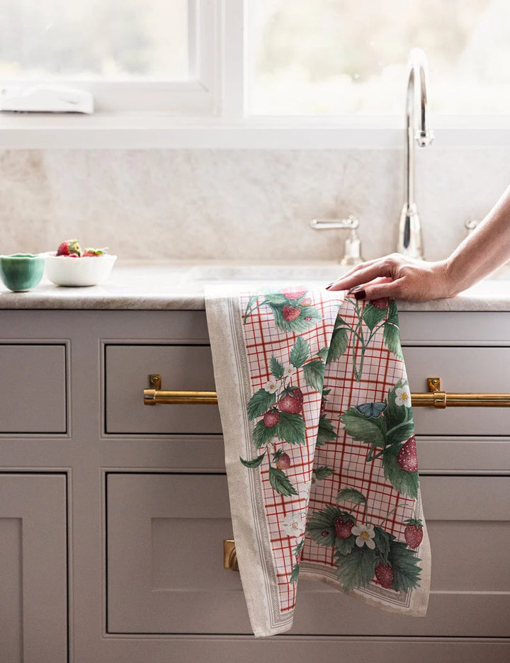 Person hanging a decorative kitchen towel with strawberry pattern on a kitchen counter.