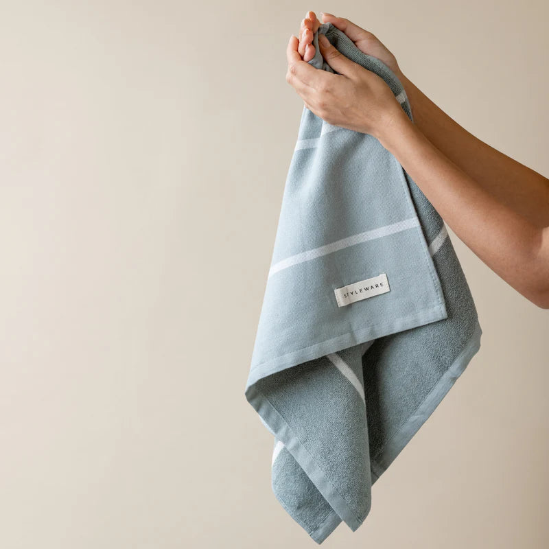 Person holding a green tea towel with a brand label against a beige background
