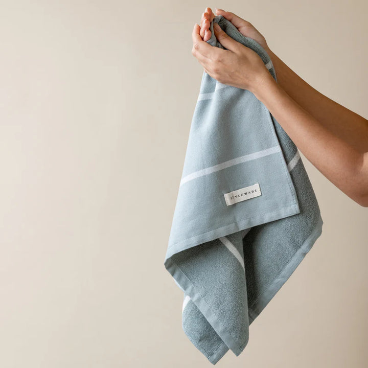 Person holding a green tea towel with a brand label against a beige background