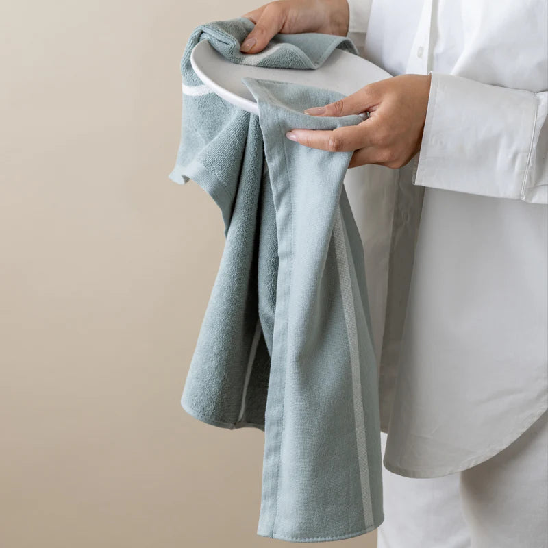 Person holding a light green tea towel over a white surface with a neutral background