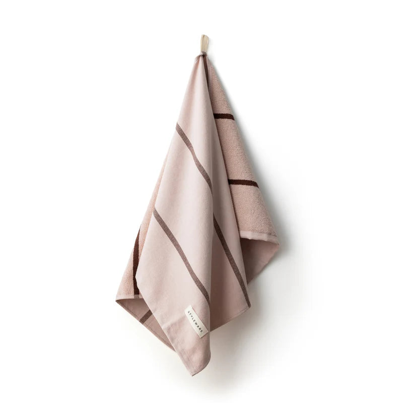 Pink towel with brown stripes hanging on a hook against a white background