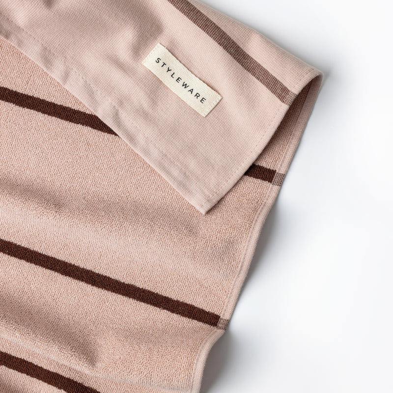 Folded pink tea towel with brown stripes and 'STYLEWARE' label on a white background