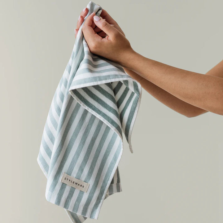 Hand holding a striped towel with 'STYLEWARE' label against a neutral background