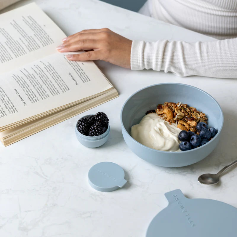 Person reading a book with a bowl of yogurt and granola on a table