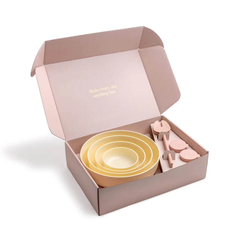 Set of nesting bowls and salad servers in a pink box .