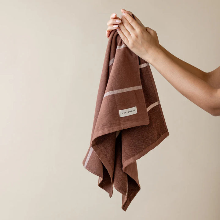 Brown towel with a brand label held by a hand against a beige background