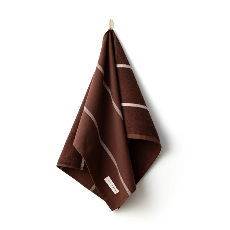 Brown tea towel with white stripes hanging on a hook against a white background