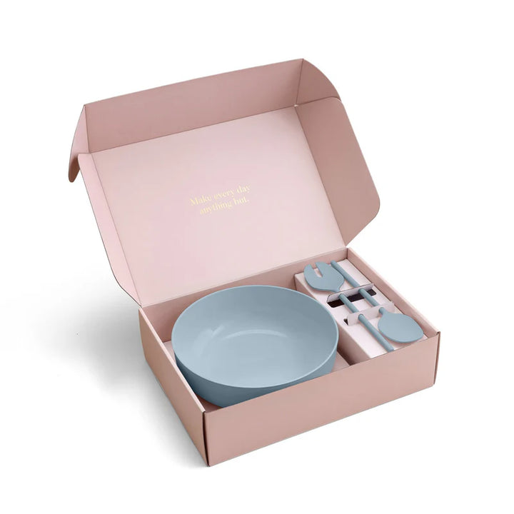 Set of blue plastic bowls and salad servers in a pink box on a white background