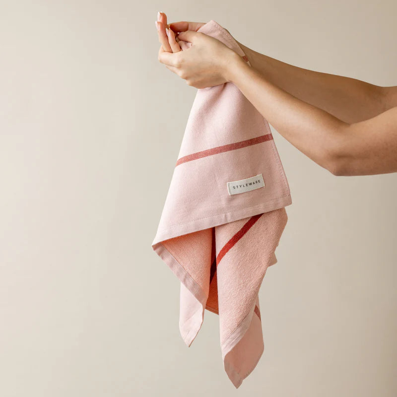 Person holding a pink towel with a brand label against a beige background