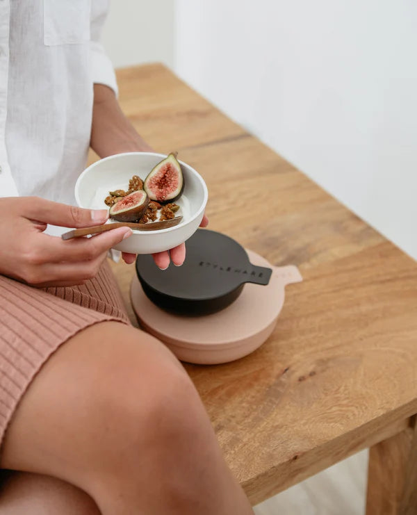 Person holding a bowl of figs with honey on a wooden table