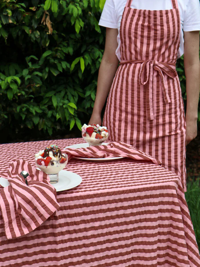 Person wearing a pink and maroon stripe apron with matching tablecloth and napkins