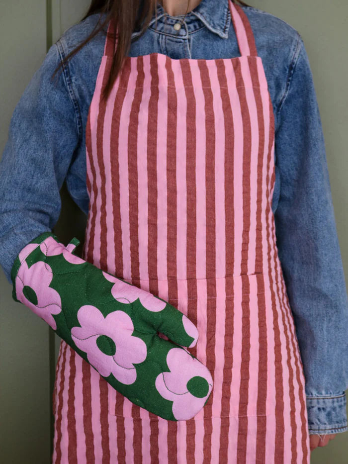 A person wearing a pink and maroon stripe apron with a pink and green oven mitt