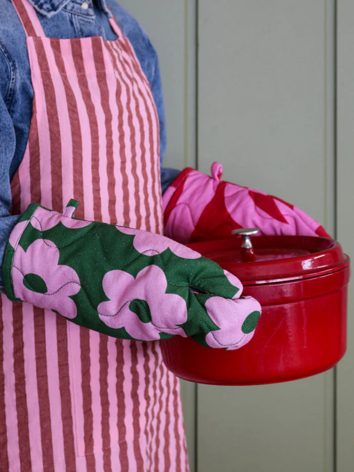 Person wear a pink and maroon stripe apron holding a red cast iron pot