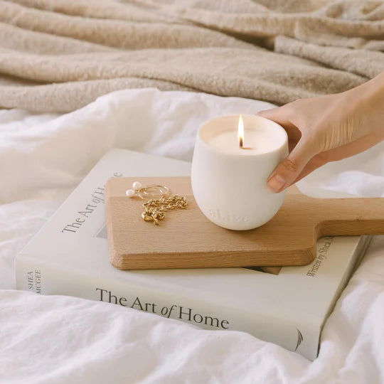 Hand holding a white candle over a book with a wooden coaster on a textured surface