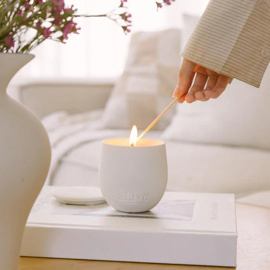 Person lighting a white candle with a wooden matchstick on a table.