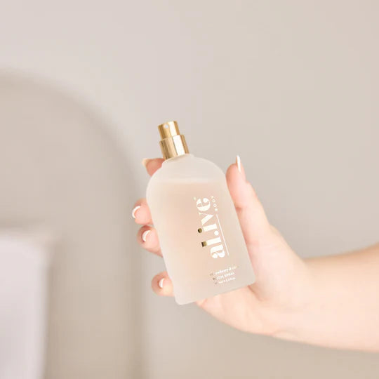 Hand holding a clear bottle with a gold cap against a neutral background