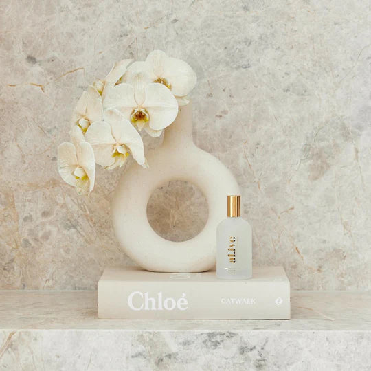 White vase with flowers and a bottle of Chloe perfume on a marble surface