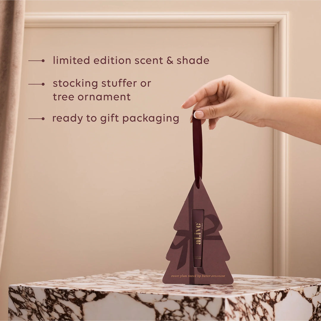 Hand holding a tree-shaped packaging with text about limited edition scent, stocking stuffer, and tree ornament.