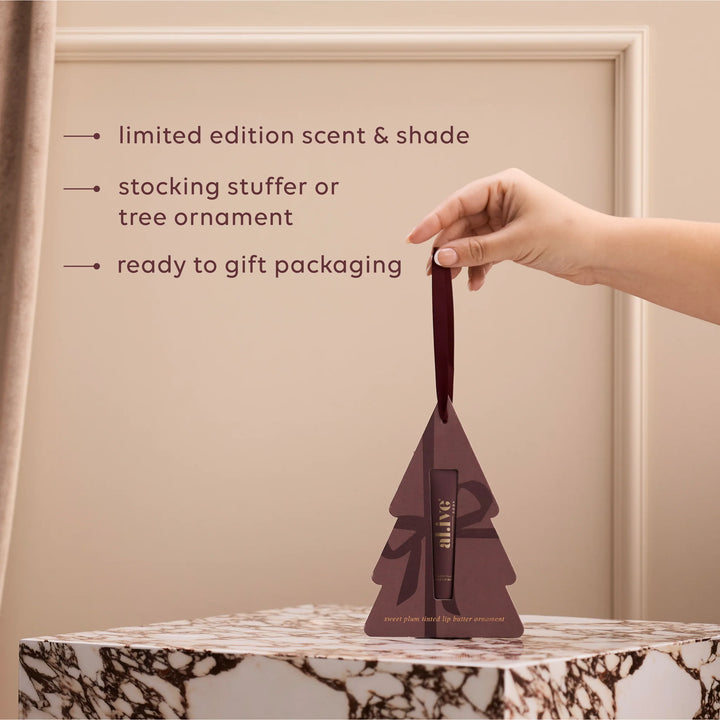 Hand holding a tree-shaped packaging with text about limited edition scent, stocking stuffer, and tree ornament.