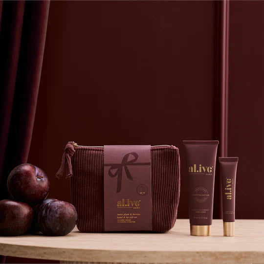 Cosmetic bag and tubes with 'alive' branding on a wooden surface against a dark red curtain.