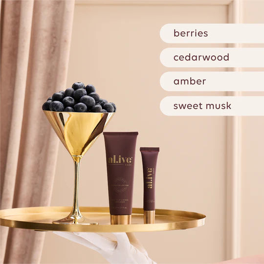 Two tubes of Al.ive body products on a gold tray with a glass of berries against a beige curtain.