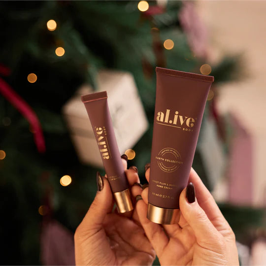 Two tubes of 'alive' hand cream and lip butter held in front of a blurred festive background