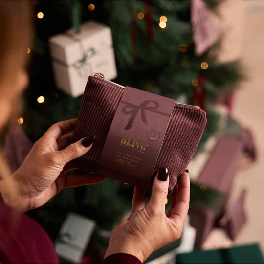 Person holding a cosmetic bag with a brand logo in front of a Christmas tree.