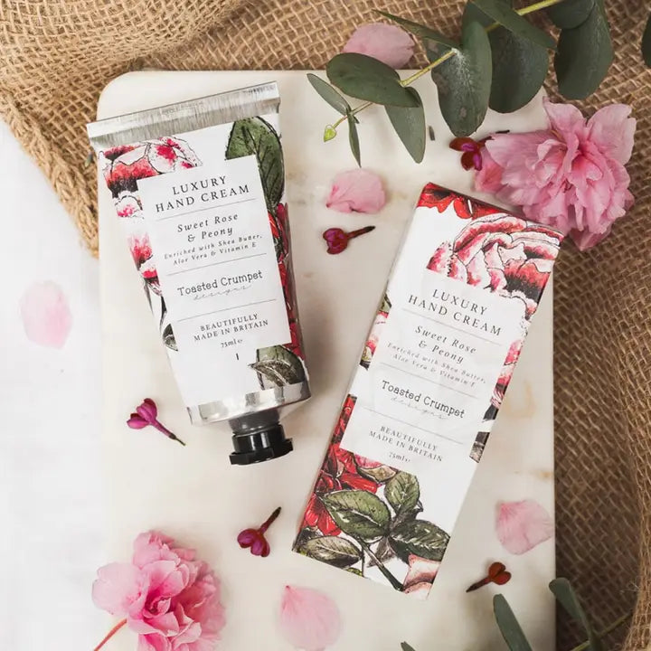A luxury hand cream tube &amp; box with floral packaging on a textured surface with flowers.