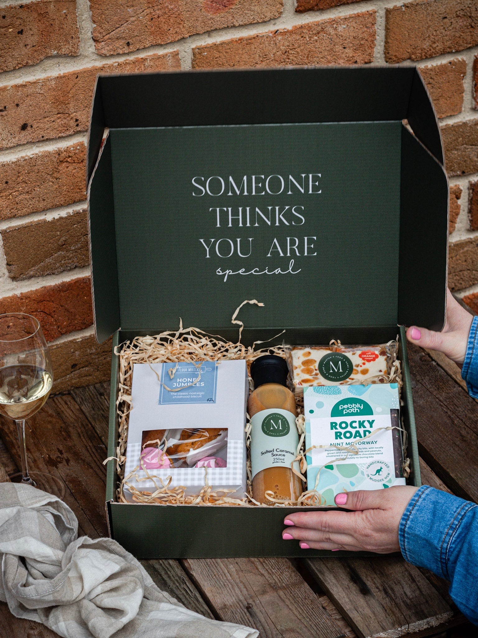 A hamper box full of sweet treats on a wooden bench with a brick background