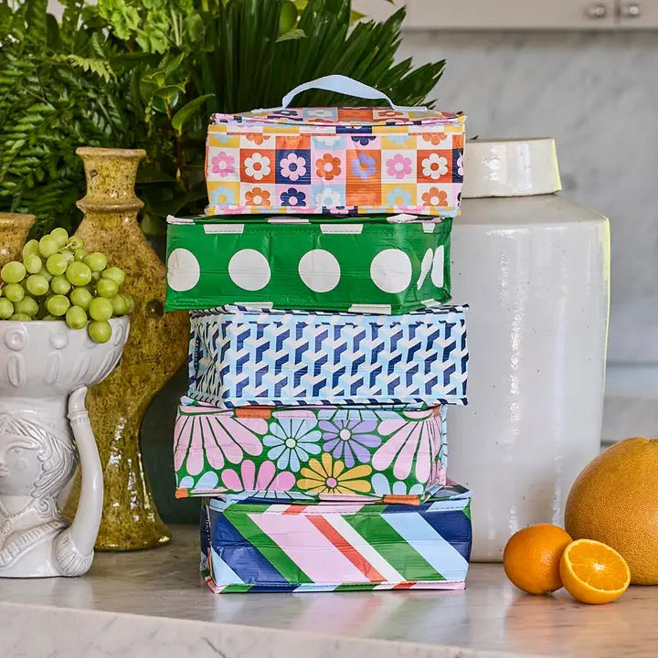 Stack of colorful patterned boxes on a kitchen counter with fruits and plants.