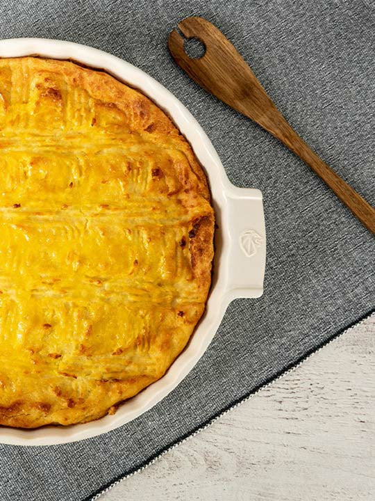 Shepherd's pie in a white dish on a gray surface with a wooden spoon.