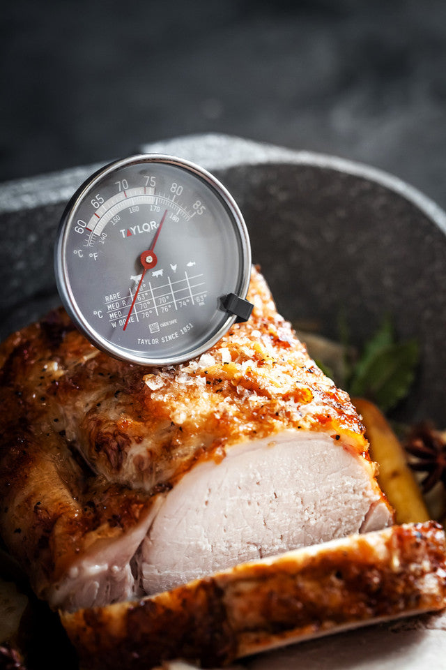 Thermometer inserted into a piece of roasted meat on a dark background