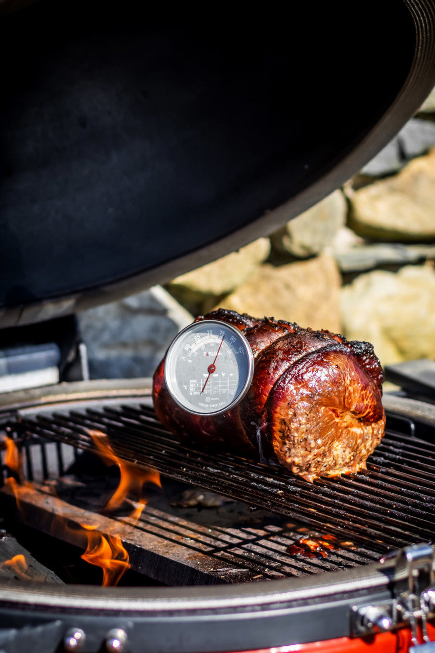 Meat on a grill with a thermometer inserted, set against a natural stone background.