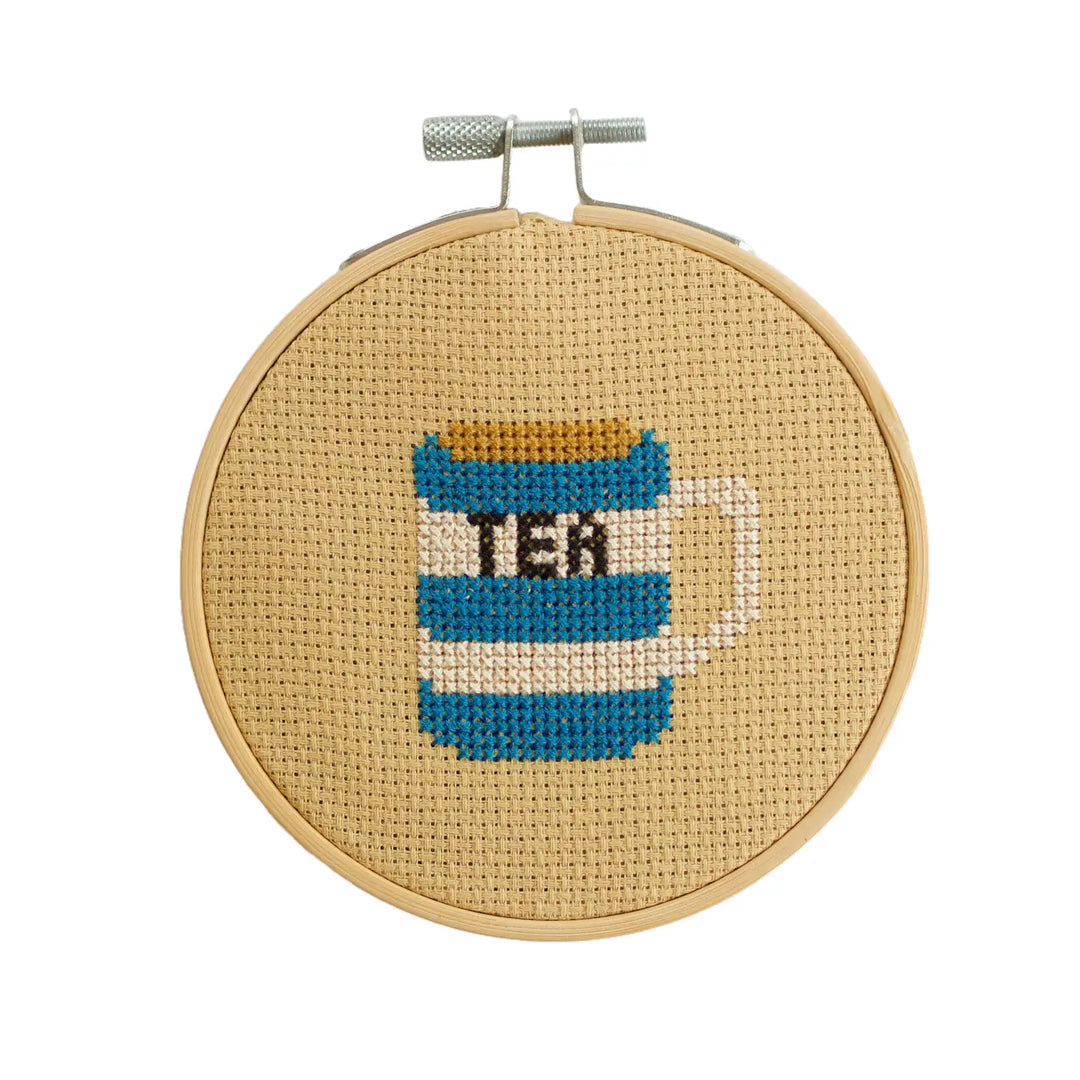 Cross-stitched tea canister design on a wooden hoop with a white background
