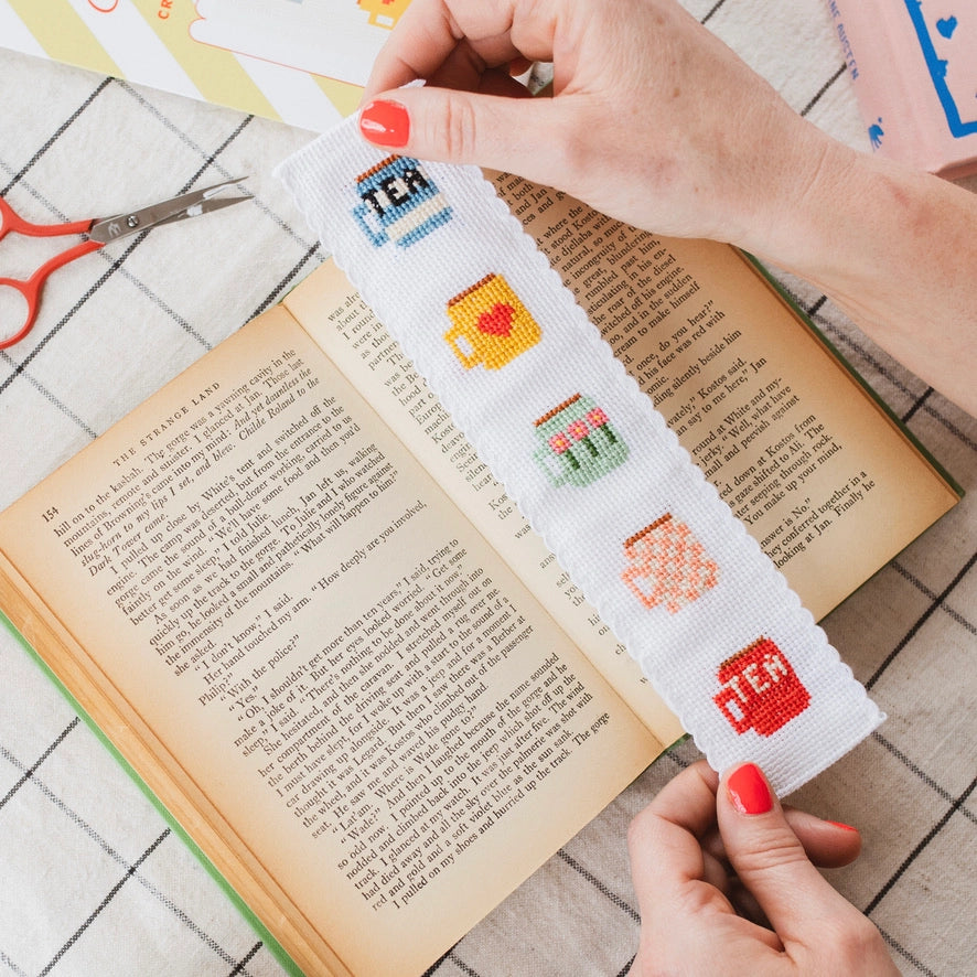 Cross-stitched bookmark with colorful designs held over an open book.
