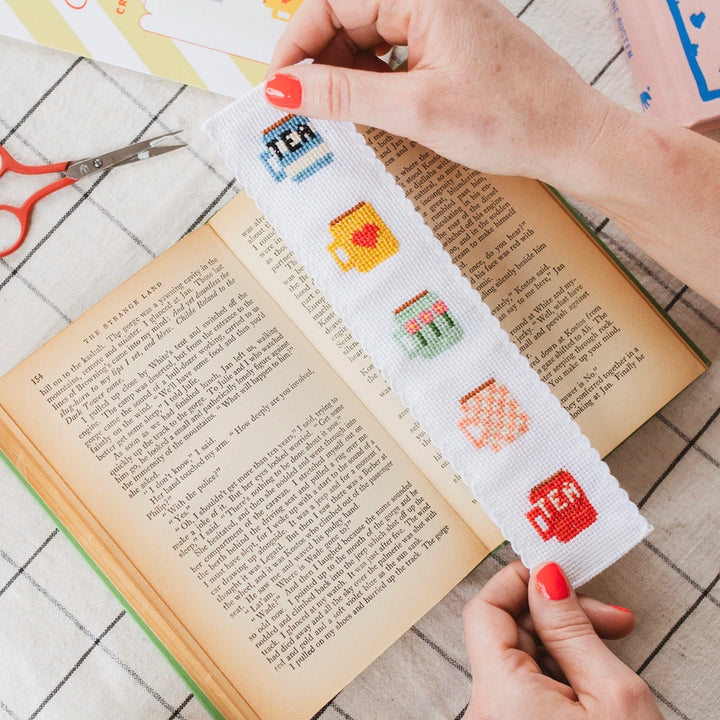 Cross-stitched bookmark with colorful designs held over an open book.