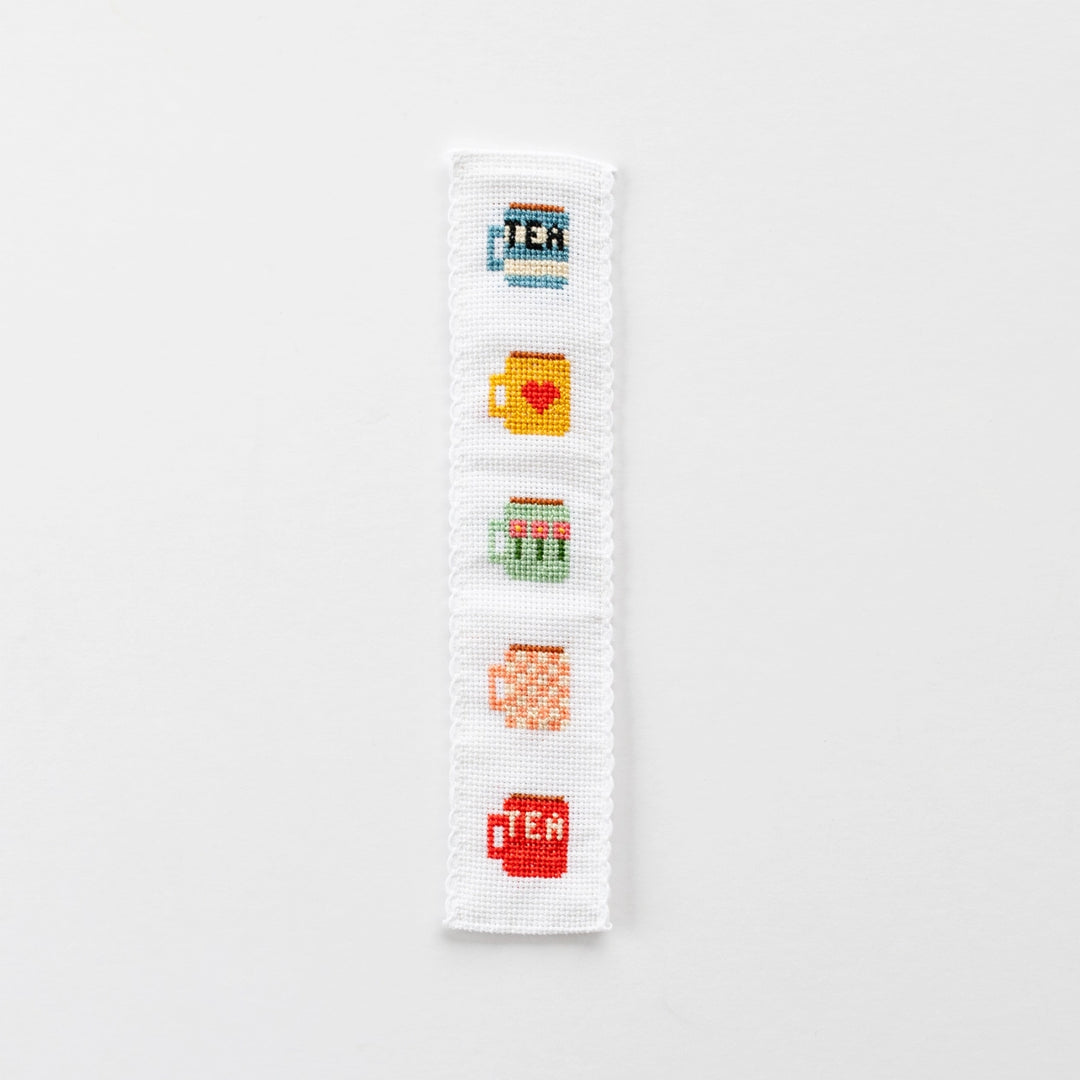 Cross-stitched bookmark with tea-themed designs on a white background
