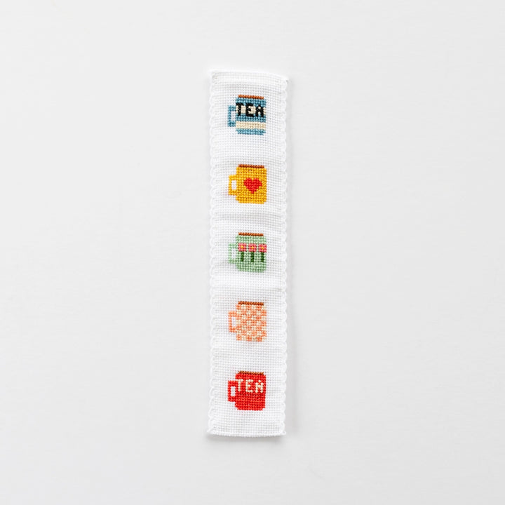 Cross-stitched bookmark with tea-themed designs on a white background