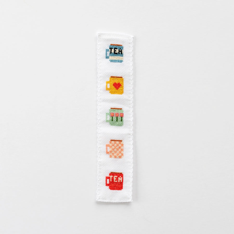 Cross-stitched bookmark with tea-themed designs on a white background