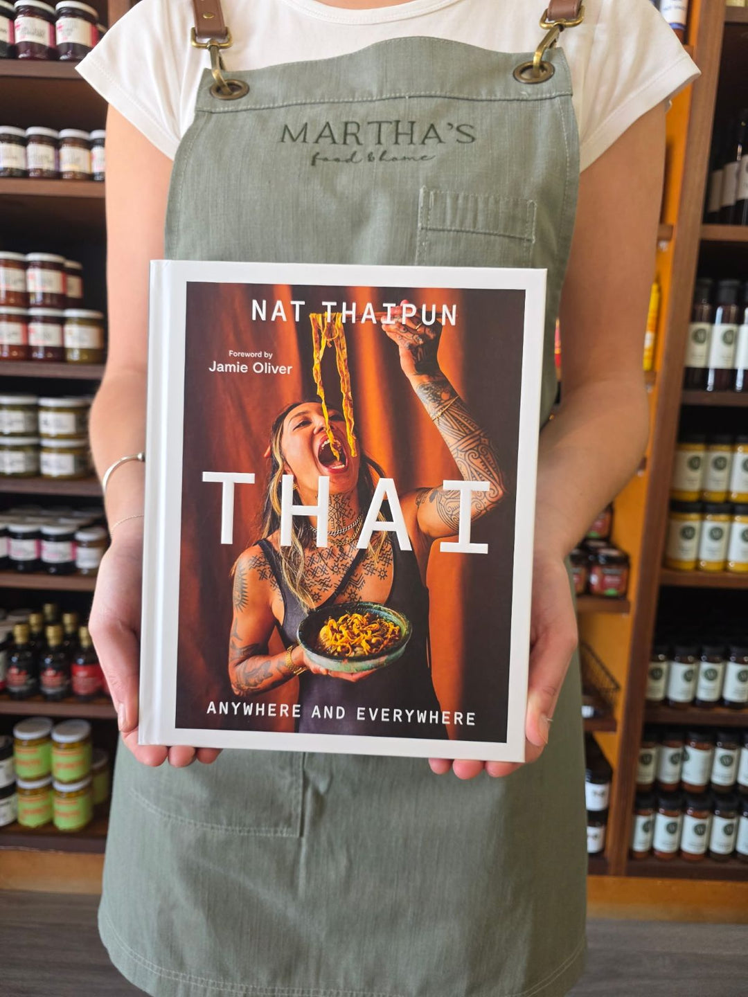 Person holding a book titled 'THAI' by Nat Thatpun in a store setting.