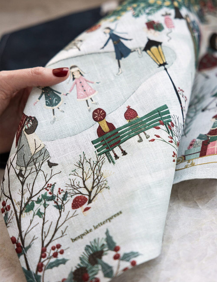 A close up of a christmas linen tea towel with a village theme 