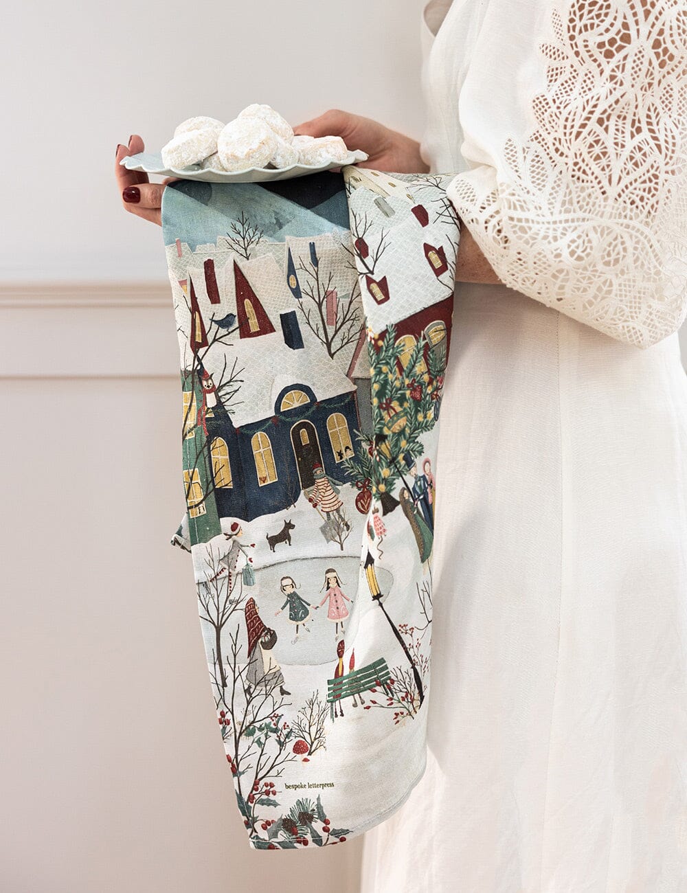 A christmas village scene linen tea towel over someones arm 