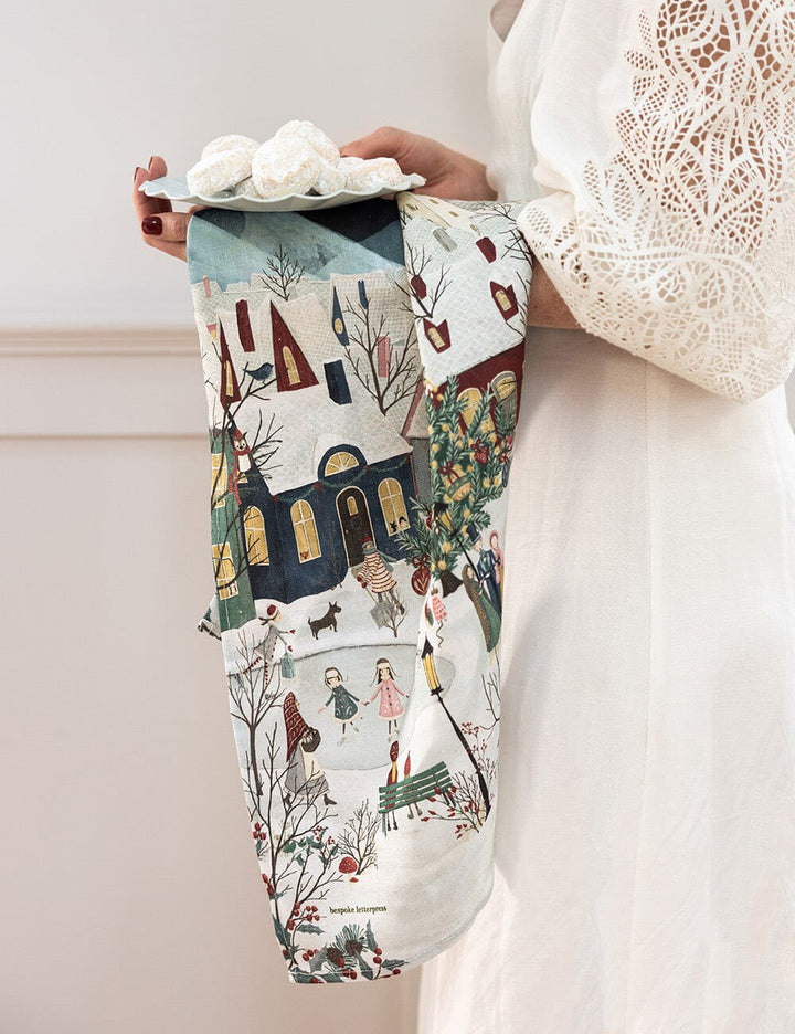 A christmas village scene linen tea towel over someones arm 